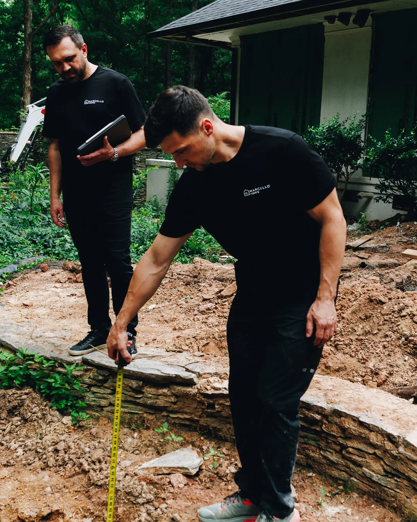 Marcello Homes builders measuring a stone retaining wall on a custom home site